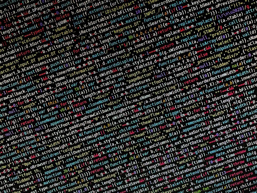 A close-up photograph of a computer screen displaying a dense block of colourful programming code. The code consists of various syntax elements, including keywords, variables, functions, and operators